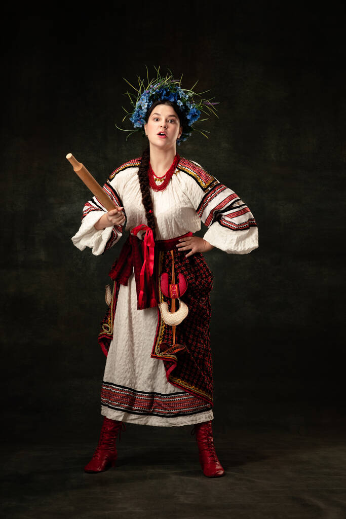 Fight for womens rights. Emotional adorable woman wearing national folk Ukrainian attire posing isolated over dark vintage background. Fashion, beauty, cultural heritage concept. - Zdjęcie, obraz