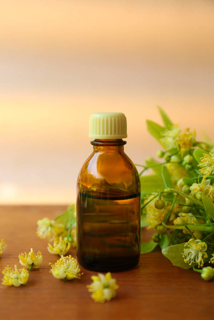 Bottle of essential oil and linden blossoms on wooden table against blurred background - Valokuva, kuva
