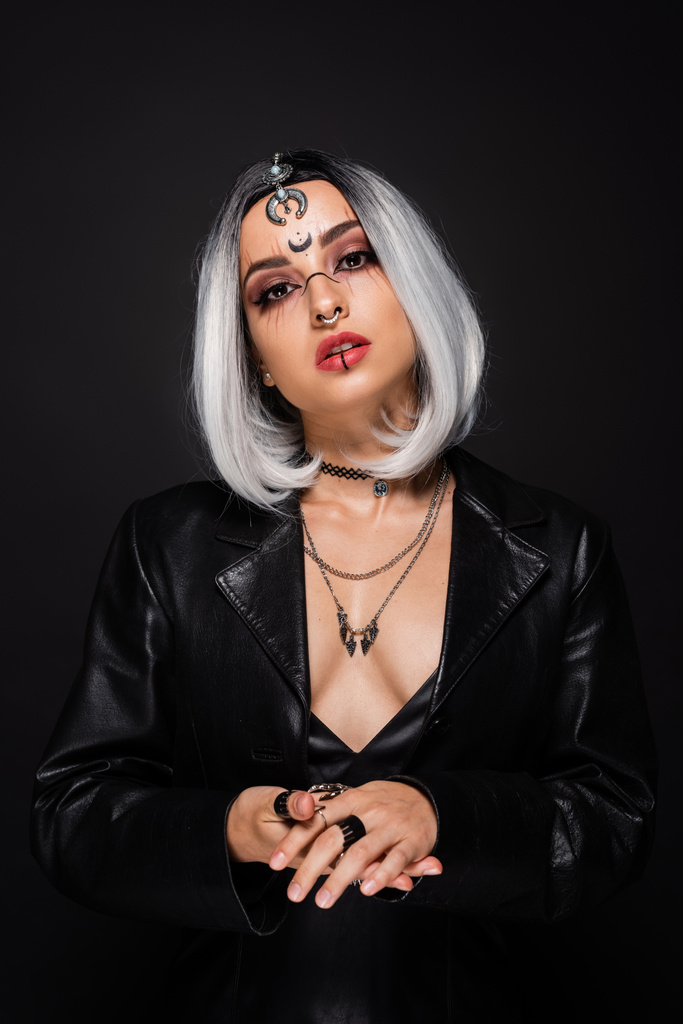 verführerische Frau in Halloween-Make-up und Lederjacke, die isoliert auf schwarz in die Kamera blickt - Foto, Bild