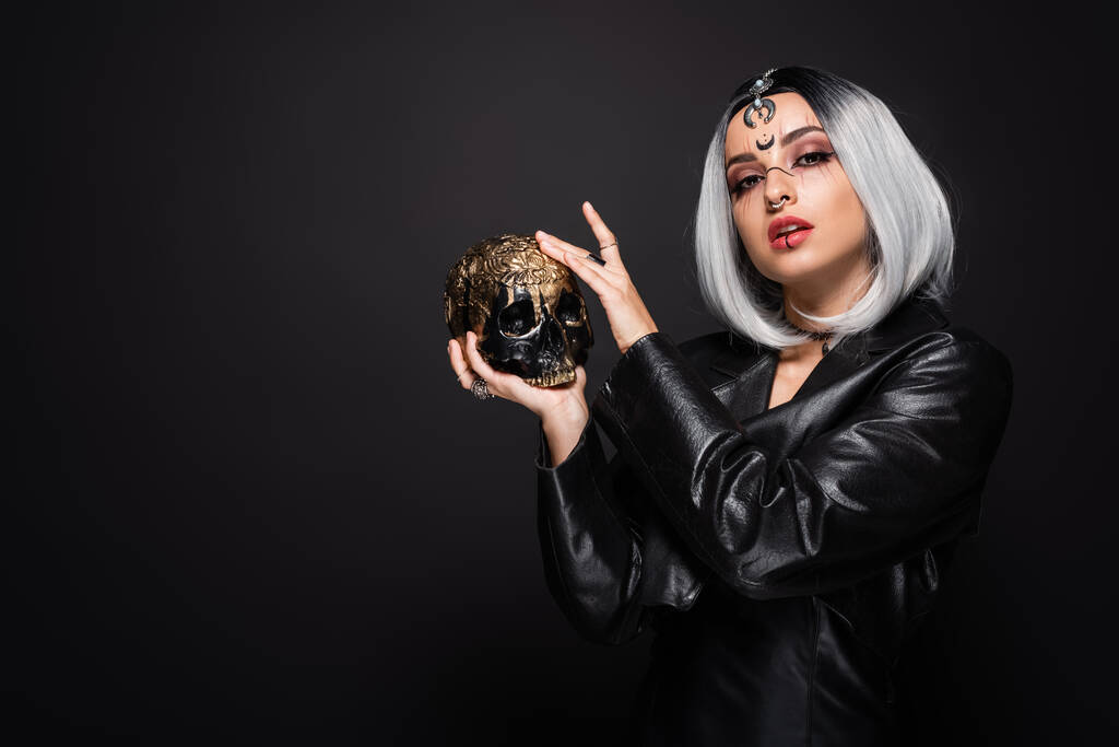 Frau in Hexenhalloween-Kostüm und Make-up posiert mit goldenem Totenkopf isoliert auf schwarz - Foto, Bild