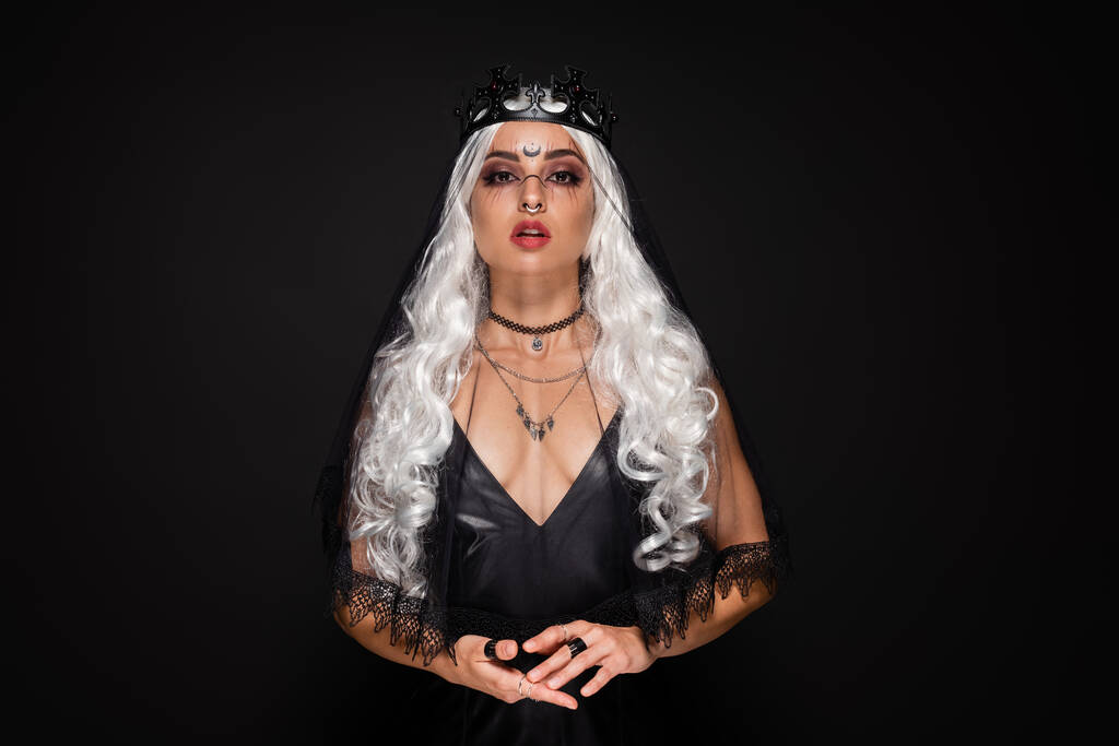 mulher loira em bruxa coroa e véu olhando para a câmera isolada no preto - Foto, Imagem