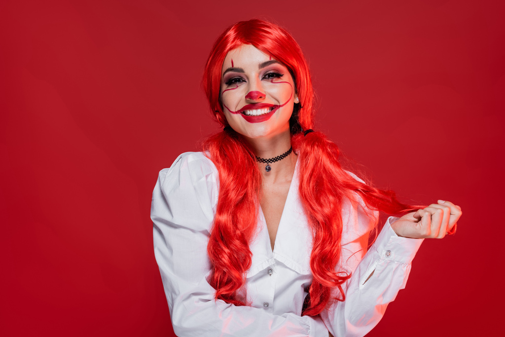 joyful woman with clown halloween makeup and bright hair isolated on red - Photo, Image