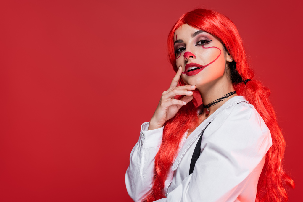 mulher ruiva pensativo com halloween maquiagem tocando rosto e olhando para a câmera isolada no vermelho - Foto, Imagem