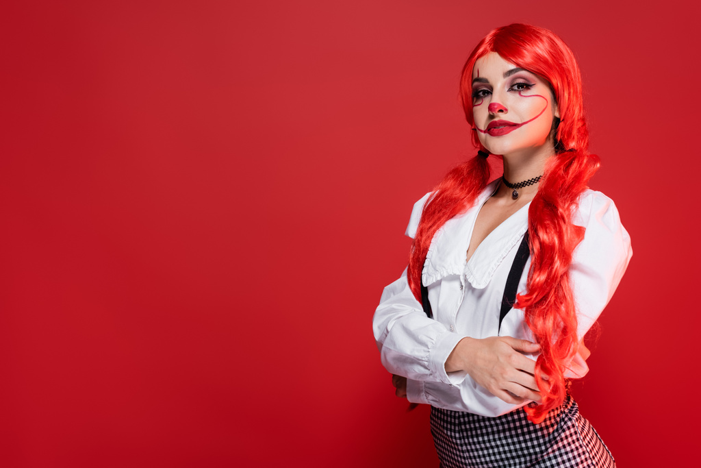 mulher com cabelos coloridos brilhantes e maquiagem halloween posando com braços cruzados isolados no vermelho - Foto, Imagem