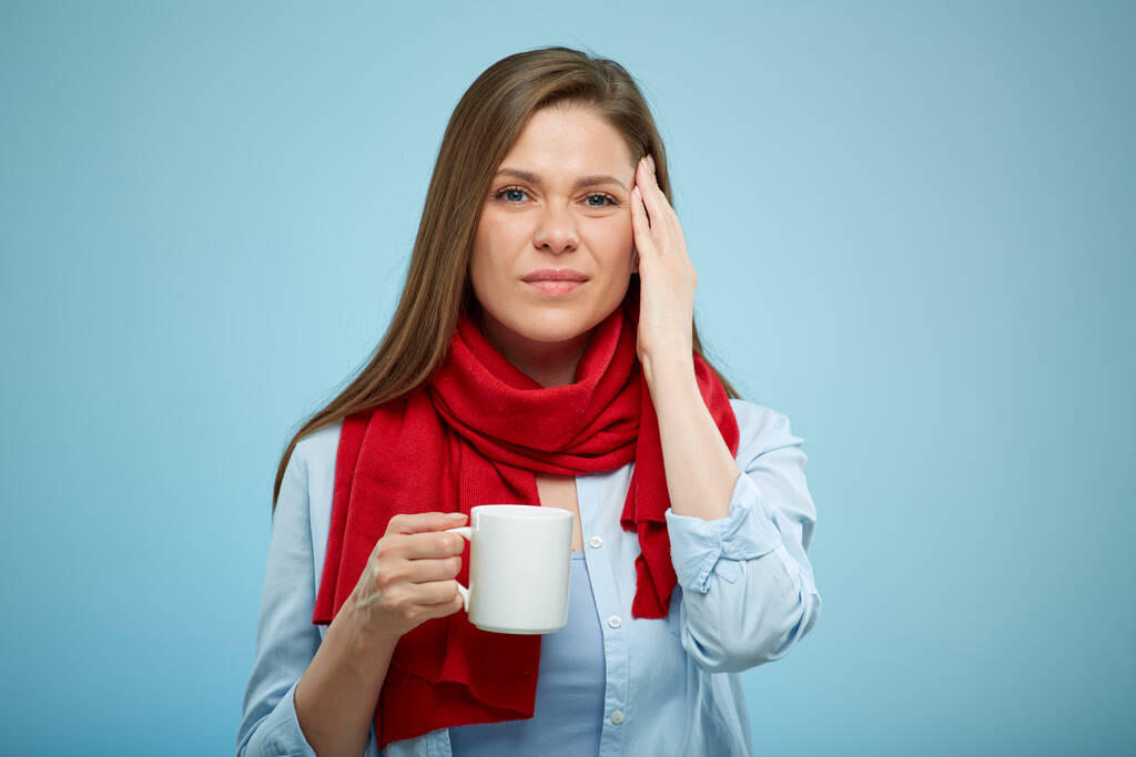 junge Frau mit Kopfschmerzen hält weiße Tasse mit Tee oder etwas Getränk in der Hand. krankes Mädchen mit rotem Schal. isoliertes Frauenporträt. - Foto, Bild
