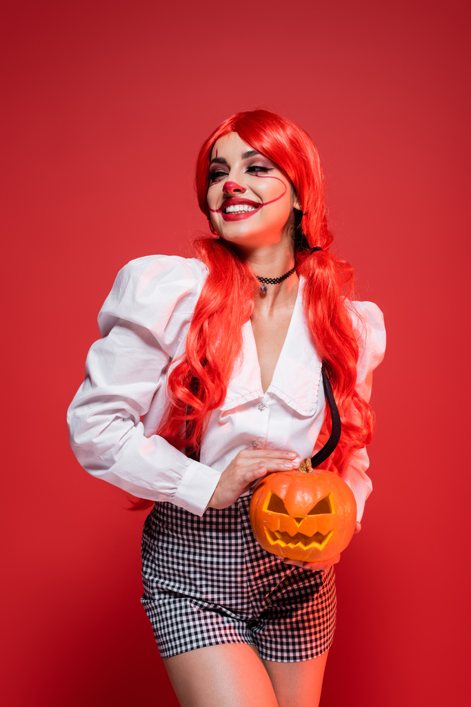happy woman in halloween makeup holding jack o lantern isolated on red - Photo, Image