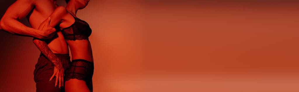 вид збоку жінки в чорній сексуальній білизні біля без сорочки чоловік на червоному тлі, банер
 - Фото, зображення