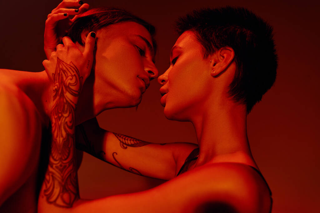 side view of passionate tattooed woman embracing and kissing young man isolated on red - Photo, Image