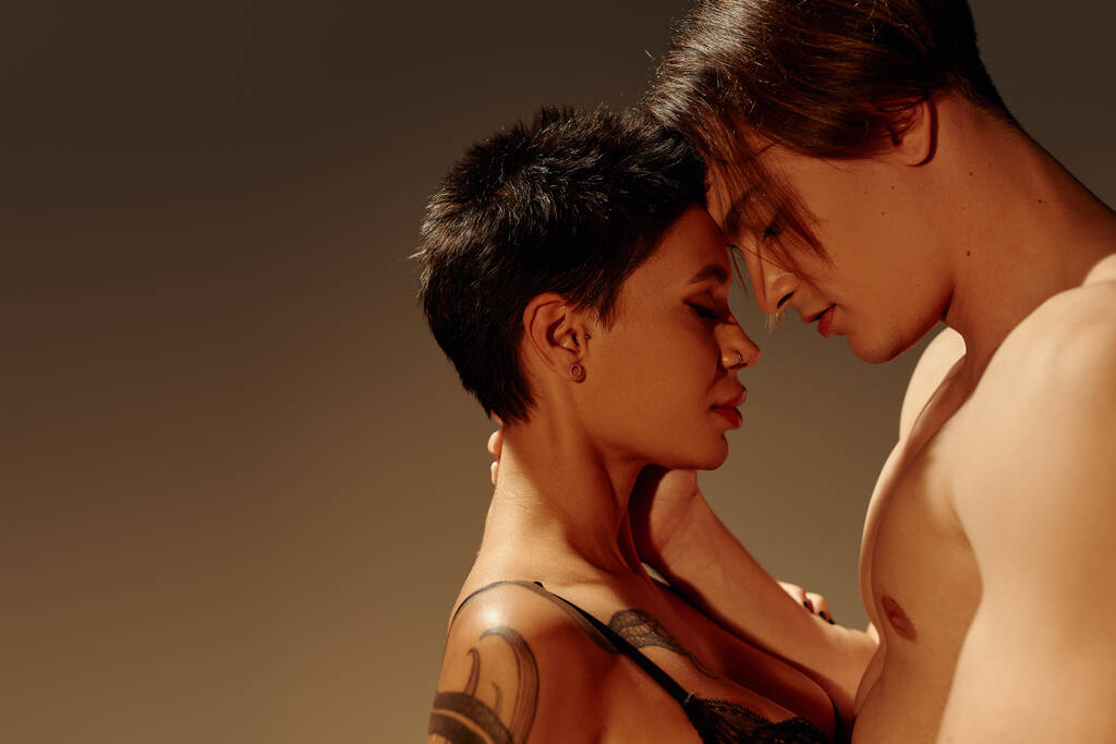 oldalnézetben szexi tetovált nő és félmeztelen férfi áll szemtől szemben zárt szemmel elszigetelt barna - Fotó, kép