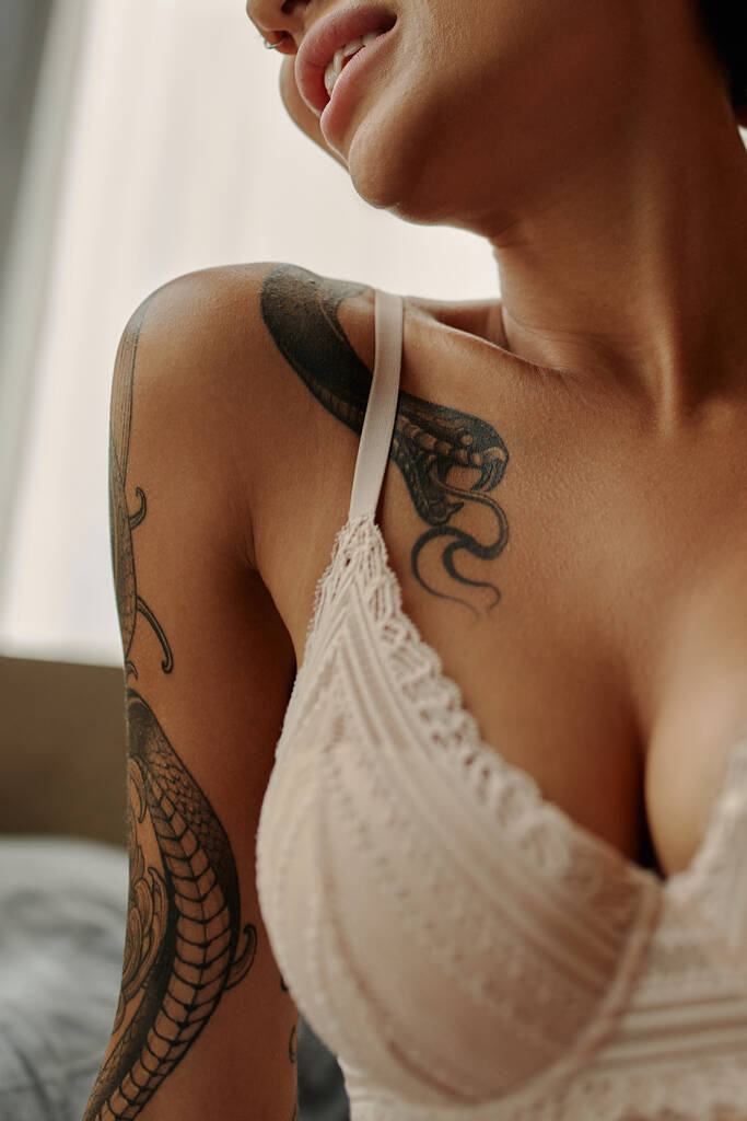 vista ritagliata della donna tatuata in reggiseno di pizzo beige a casa - Foto, immagini