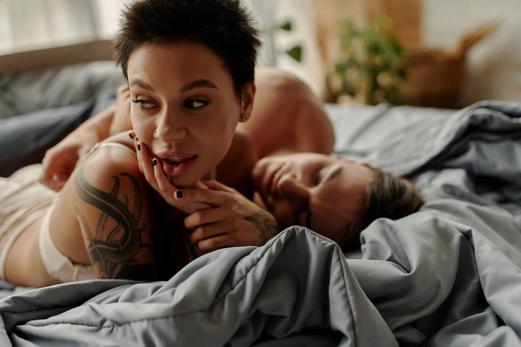 Соблазнительная женщина в нижнем белье лежит рядом с размытым парнем на кровати  - Фото, изображение