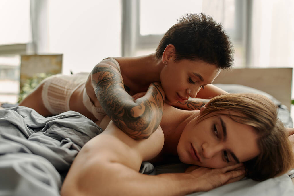 Молодая татуированная женщина лежит на спине мускулистого парня в спальне  - Фото, изображение