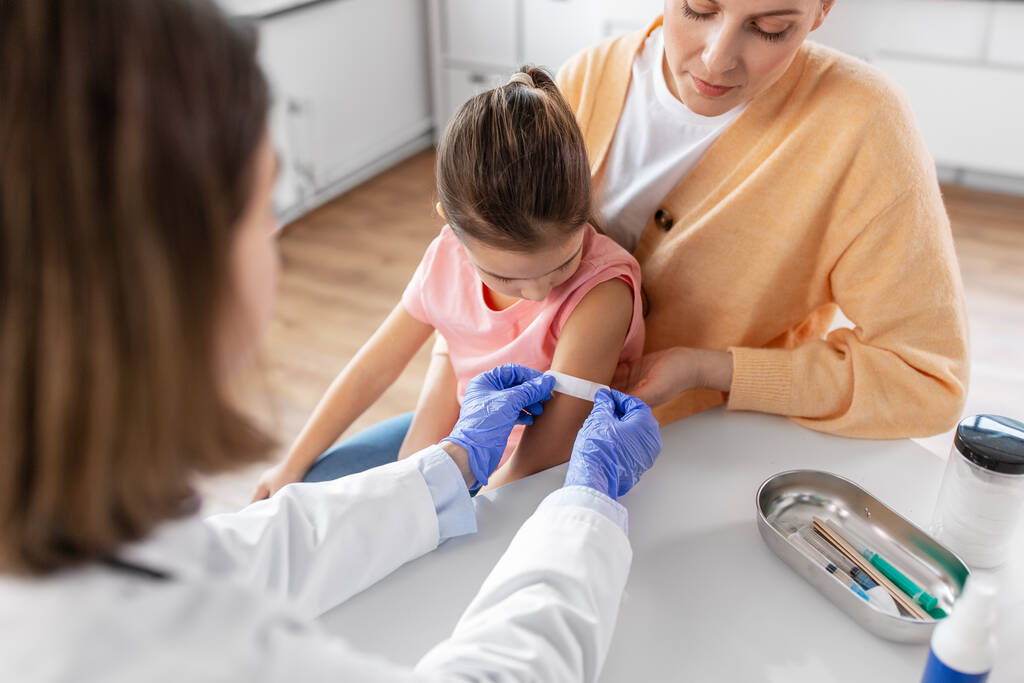 İlaç, sağlık ve pediatri konsepti - kadın doktor ya da çocuk doktoru küçük bir kızın annesinin klinikteki koluna tedavi bandı yapıştırıyor - Fotoğraf, Görsel