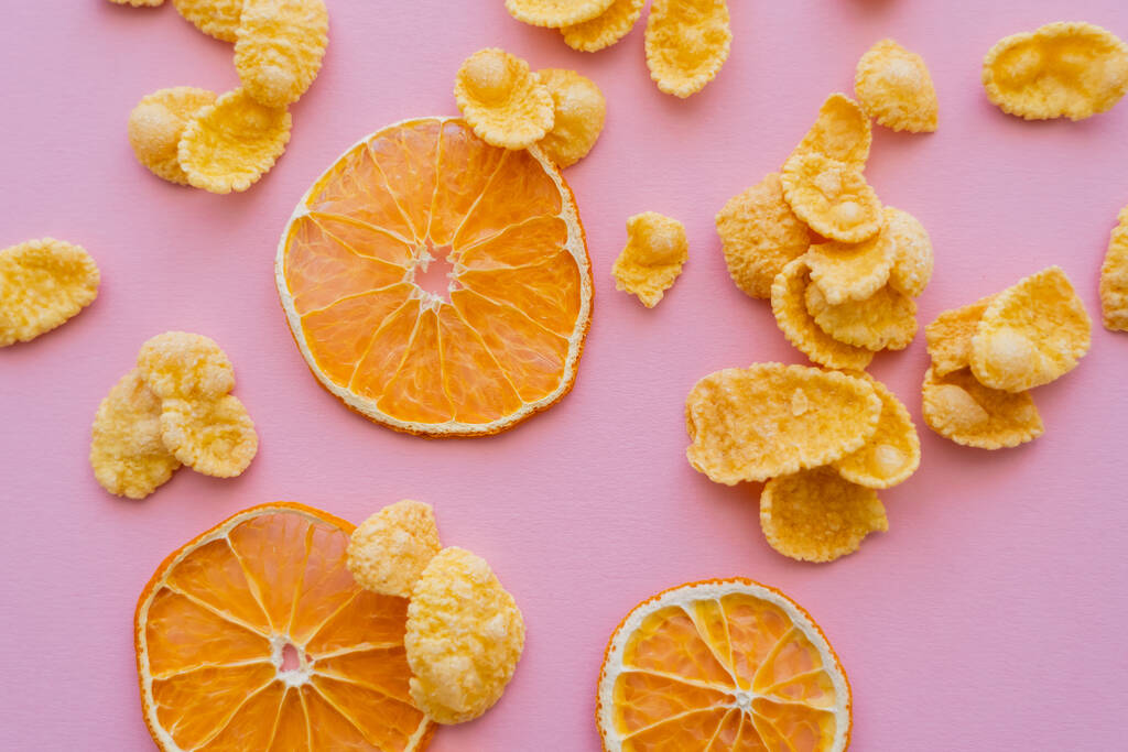 vista superior de naranjas secas cerca de hojuelas de maíz sobre fondo rosa - Foto, Imagen