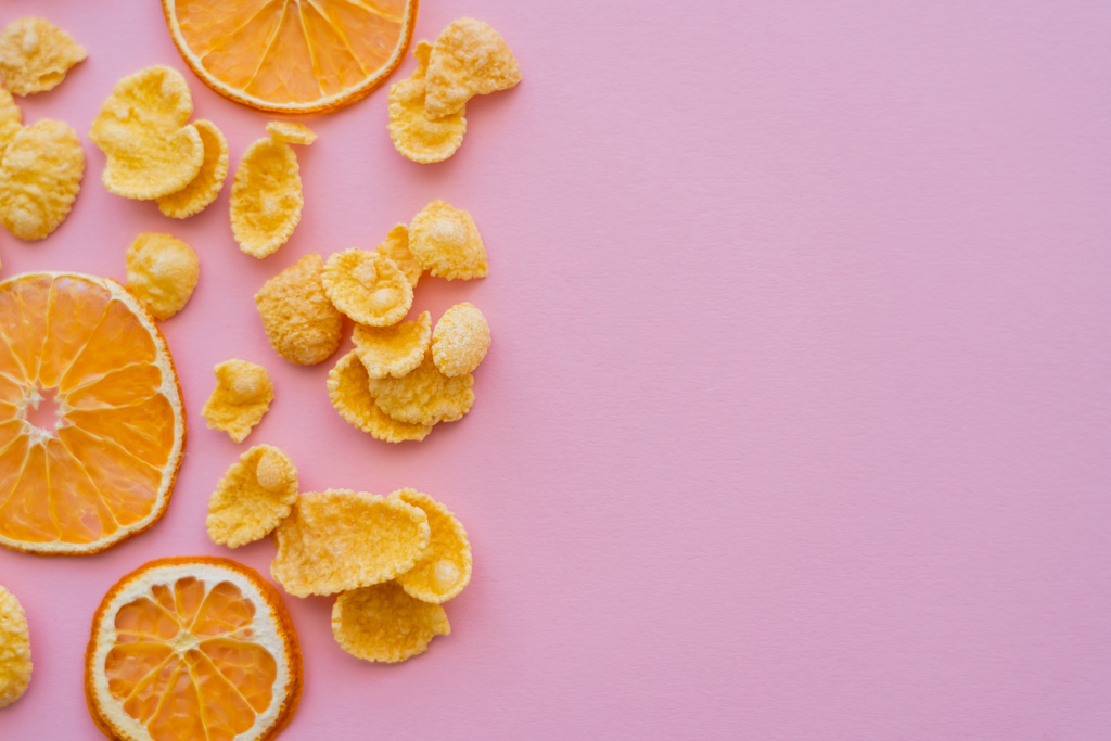 ylhäältä näkymä kuivattuja appelsiineja lähellä maukkaita maissihiutaleita vaaleanpunaisella taustalla - Valokuva, kuva