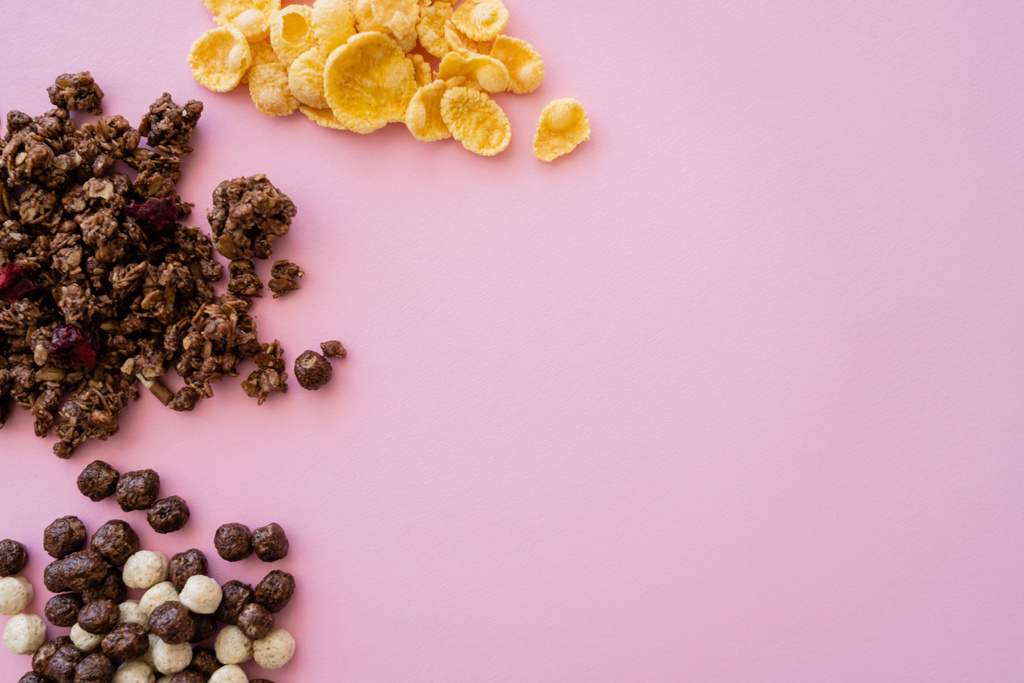 вид сверху кукурузных хлопьев возле зерновых шариков с ванильным и шоколадным вкусами и мюсли, выделенных на розовом - Фото, изображение