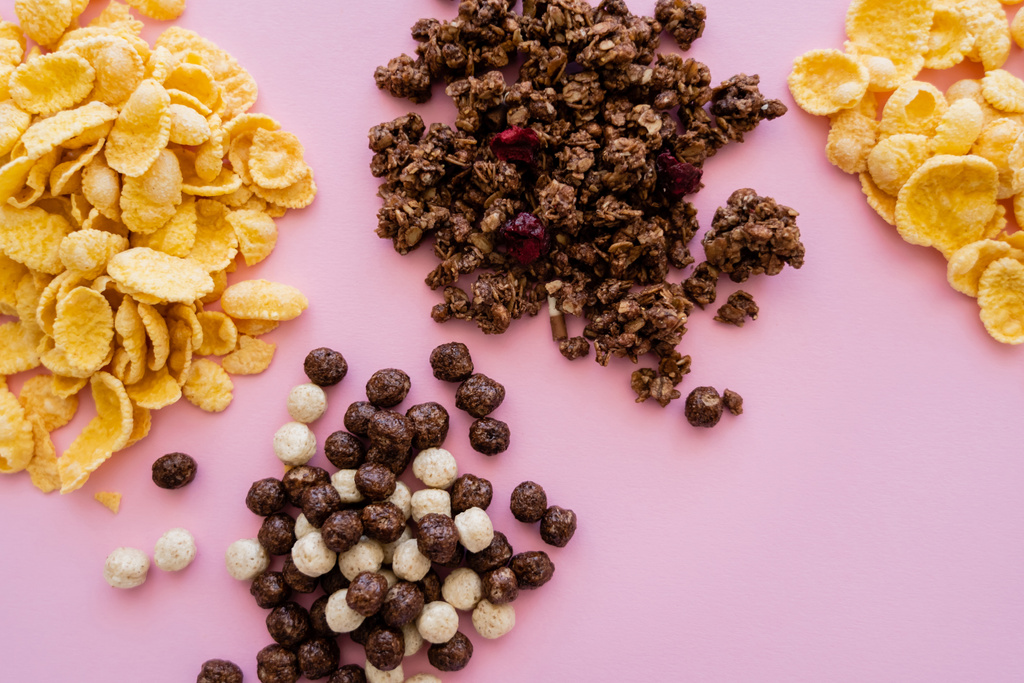 κορυφαία άποψη των νιφάδων καλαμποκιού κοντά σε μπάλες δημητριακών με γεύσεις βανίλιας και σοκολάτας και νόστιμη γκρανόλα που απομονώνονται σε ροζ - Φωτογραφία, εικόνα