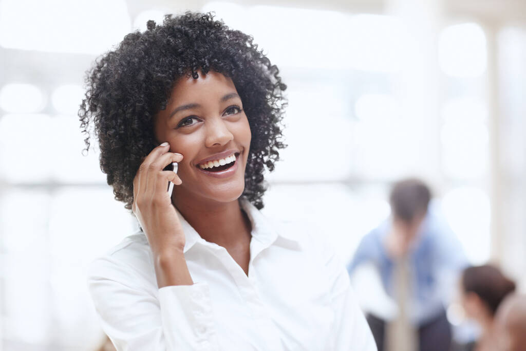 Üzleti hívás fogadása. Egy afrikai nő használja a mobilját az irodában a kollégáival a háttérben. - Fotó, kép