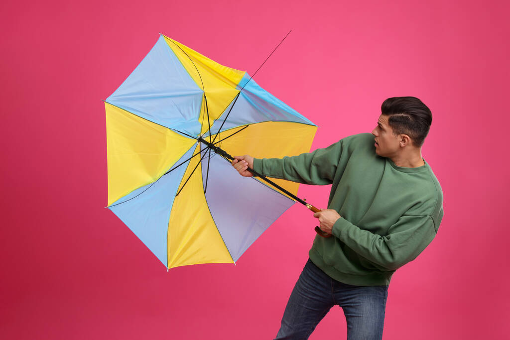 Muž s deštníkem chycený v poryvu větru na růžovém pozadí - Fotografie, Obrázek