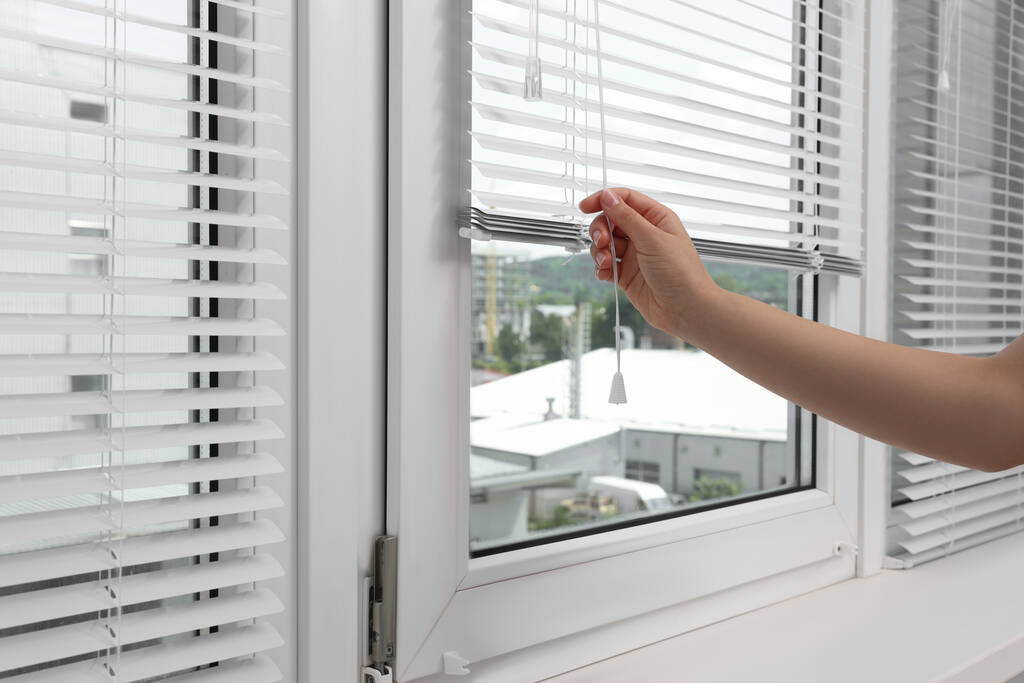 Woman opening horizontal blinds on window indoors, closeup - Foto, imagen