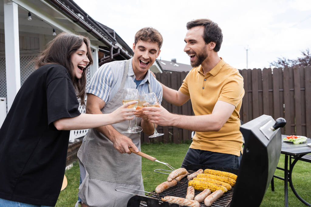 Pozytywne przyjaciele toasting z winem w pobliżu grilla BBQ na podwórku  - Zdjęcie, obraz