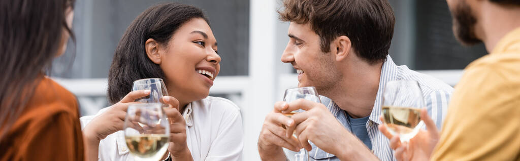 幸せな二人種間の女性がワインを飲みながら裏庭で友達を見て - 写真・画像
