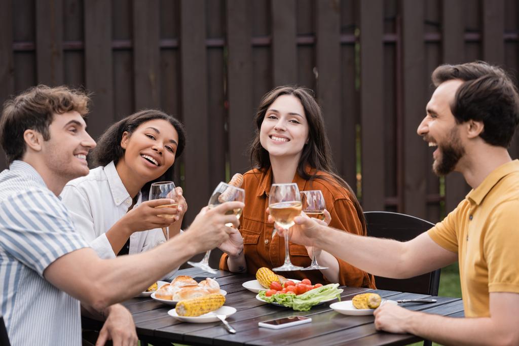 amis multiethniques joyeux cliquetis verres avec du vin et déjeuner pendant la fête barbecue  - Photo, image