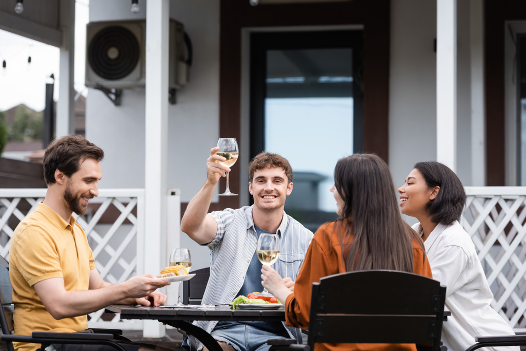 裏庭でのbbqパーティー中に異人種間の友人の近くでワインのグラスを上げる幸せな男  - 写真・画像