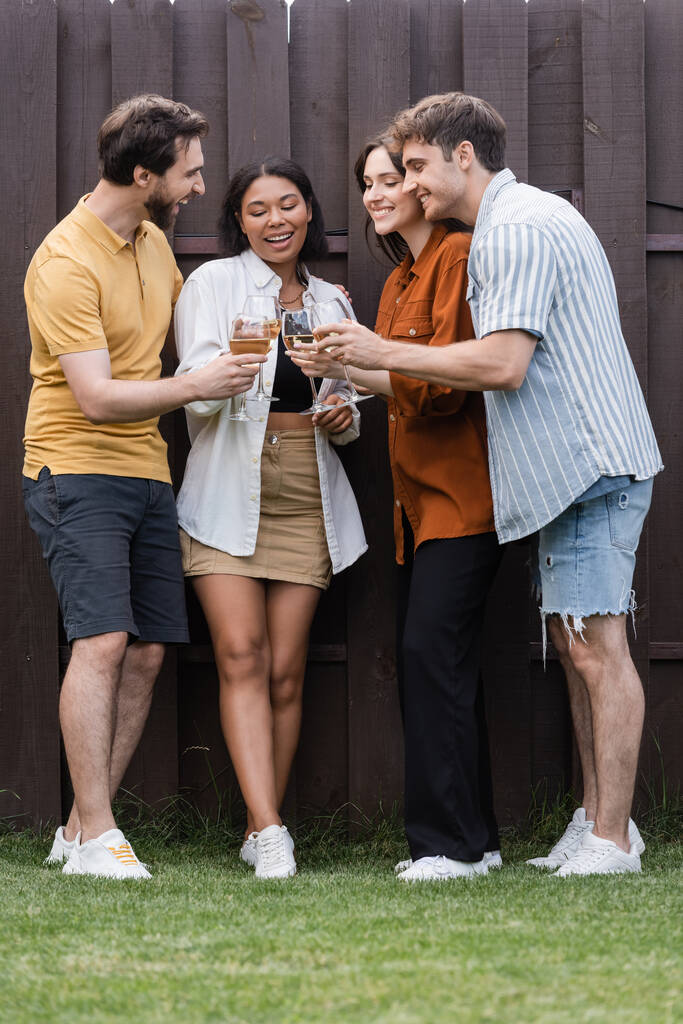 повна довжина щасливих міжрасових друзів смердить келихами з вином, стоячи біля паркану на задньому дворі
 - Фото, зображення