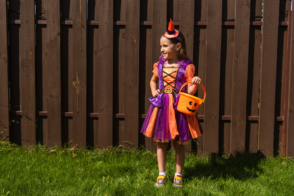 Mädchen in Clownskostüm steht mit Halloween-Eimer und schaut weg - Foto, Bild