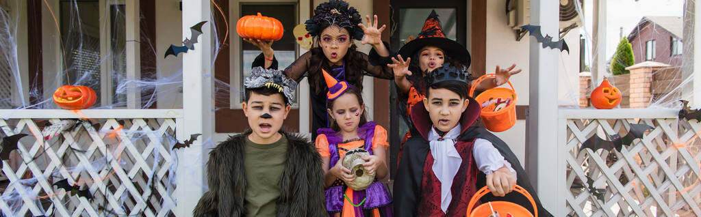 filles montrant des gestes effrayants près d'amis multiethniques en costumes d'Halloween, bannière - Photo, image