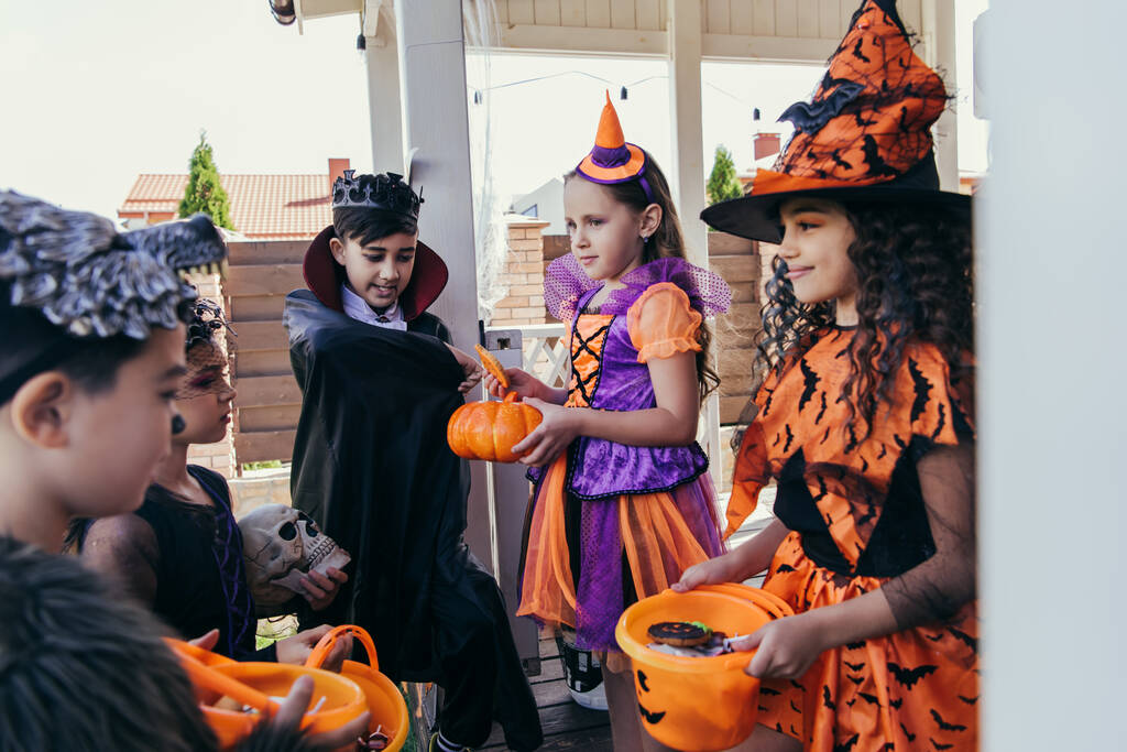 Sonriendo niños multiétnicos sosteniendo cubos y calabaza durante la celebración de Halloween al aire libre   - Foto, Imagen