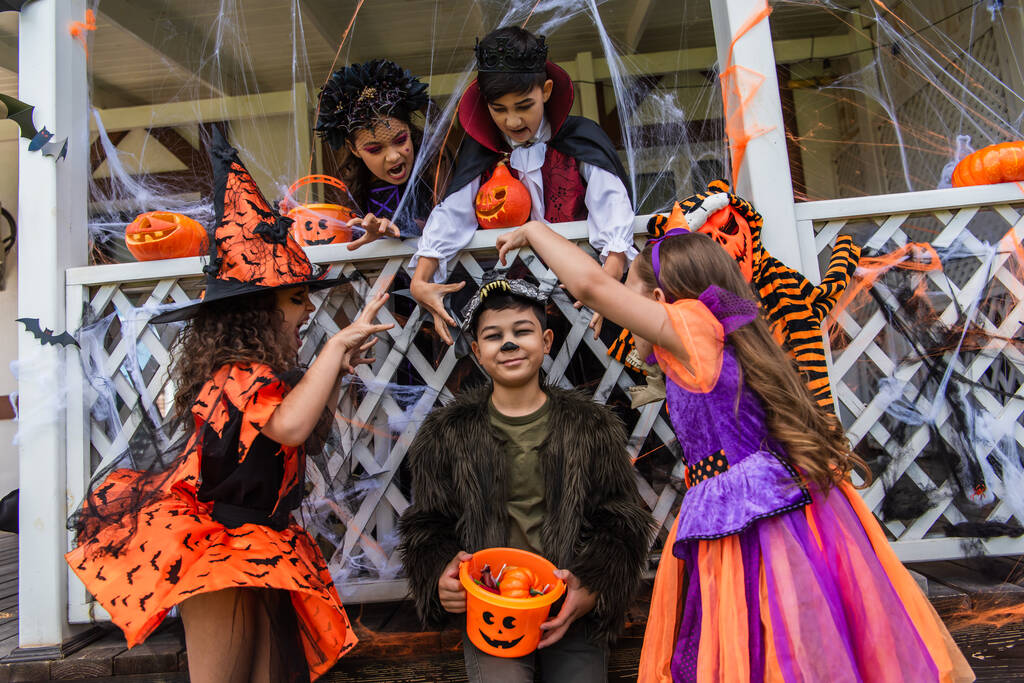 Preteen děti v halloween kostýmy grimasování poblíž asijské přítel s vědro venku  - Fotografie, Obrázek