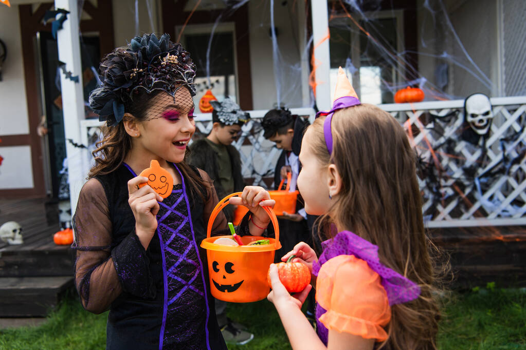 усміхнена дівчина тримає відро на Хеллоуїн з цукерками біля друга з гарбузом на задньому дворі
  - Фото, зображення