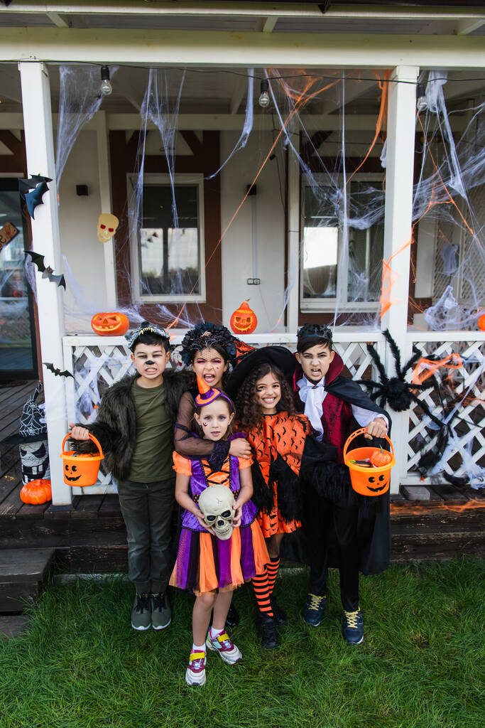 Двенадцать многонациональных друзей гримасируют перед камерой во время празднования Хэллоуина на заднем дворе дома  - Фото, изображение