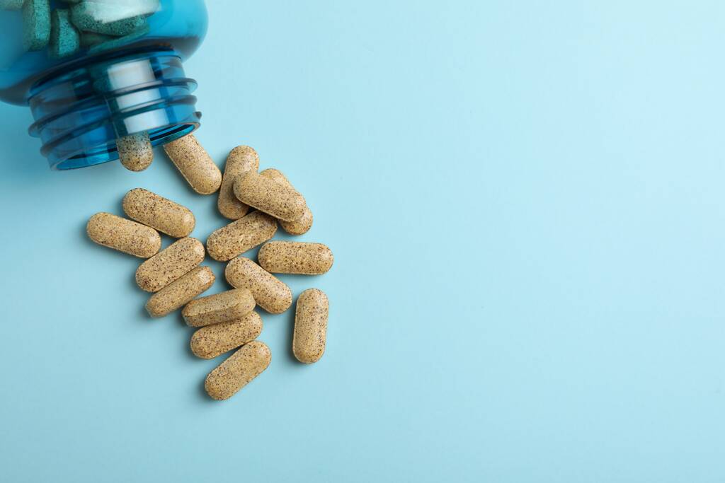 Frasco virado com pílulas de suplemento dietético em fundo azul claro, flat lay. Espaço para texto - Foto, Imagem