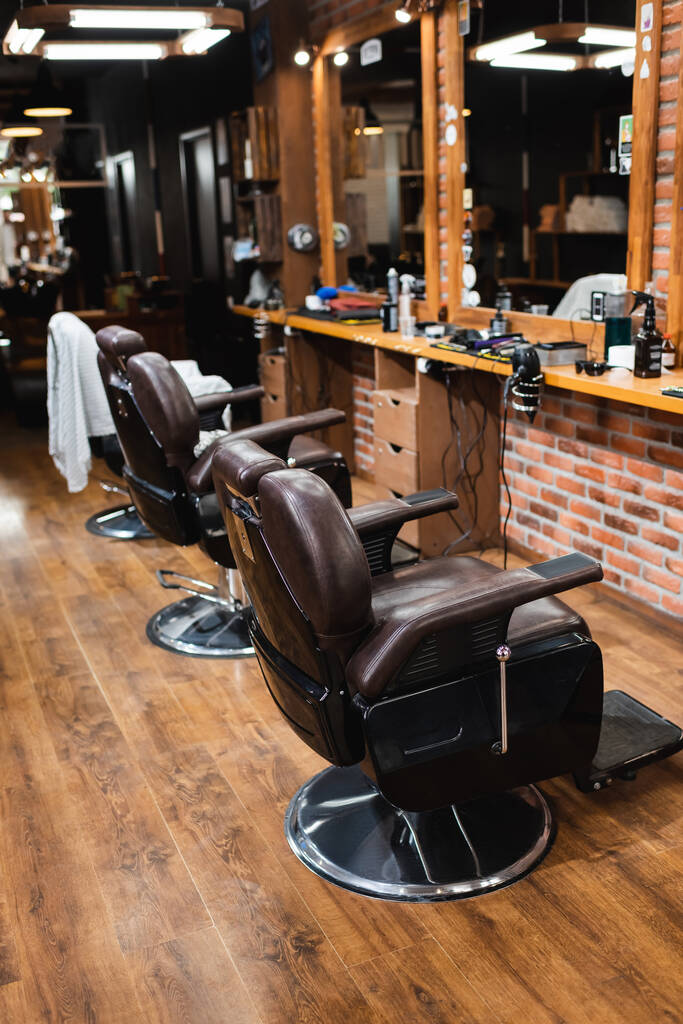 comfortabele fauteuils in de buurt van spiegels en kappers in barbershop - Foto, afbeelding