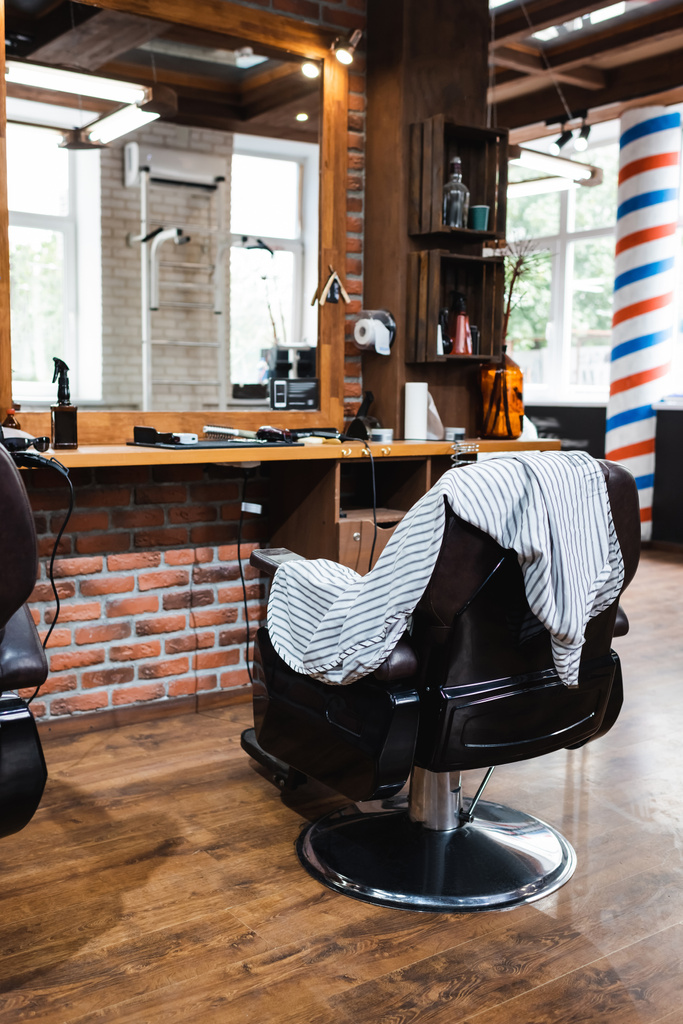 fauteuil ergonomique et cape de coiffure près du miroir dans le salon de beauté - Photo, image