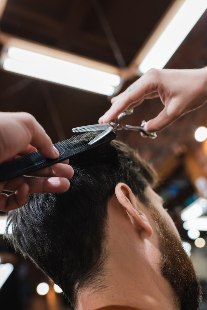 Friseur schneidet Haare eines brünetten Mannes mit dünner Schere - Foto, Bild