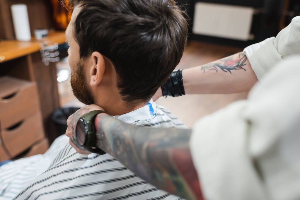 barbiere sfocato mettendo il mantello di parrucchiere sull'uomo bruna - Foto, immagini
