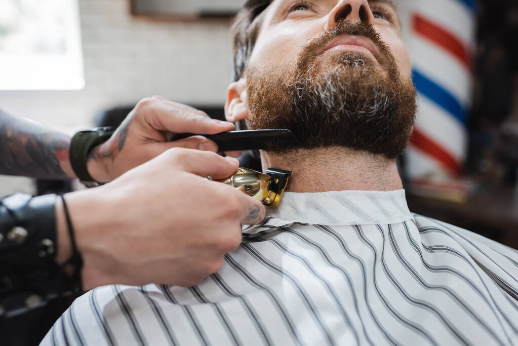 parrakas mies lähellä kampaaja leikkaamalla hänen kaulaansa hiukset leikkuri parturissa - Valokuva, kuva