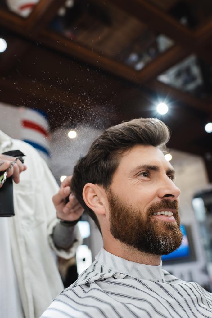barna férfi szakállas mosolygós közel borbély alkalmazása hajlakk - Fotó, kép