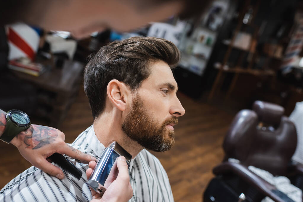 brunette bearded man near barber shaving his neck with electric razor - Photo, Image