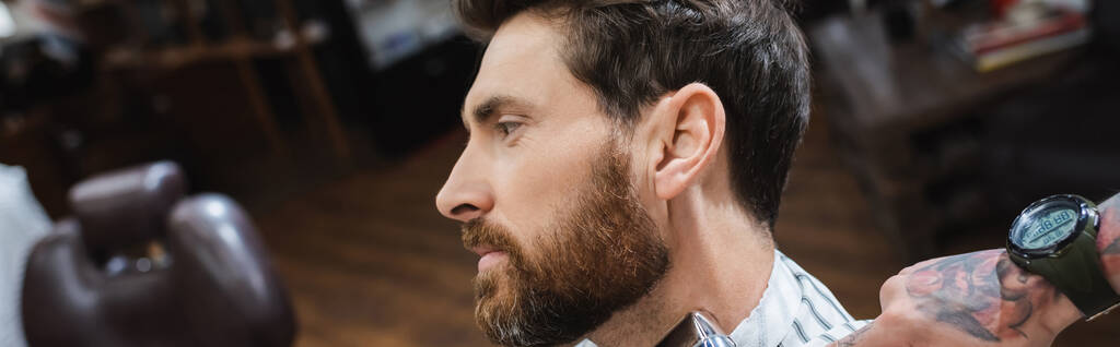 puolella näkymä brunette parrakas mies lähellä tatuoitu kampaaja parturissa, banneri - Valokuva, kuva