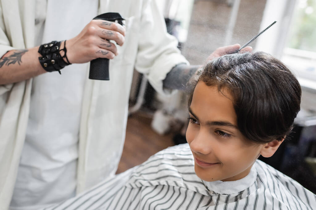 tatuato barbiere applicare lacca sui capelli sorridente adolescente cliente - Foto, immagini
