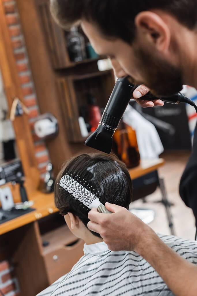 Coiffeur flou peigner et sécher les cheveux d'un adolescent dans un salon de beauté  - Photo, image
