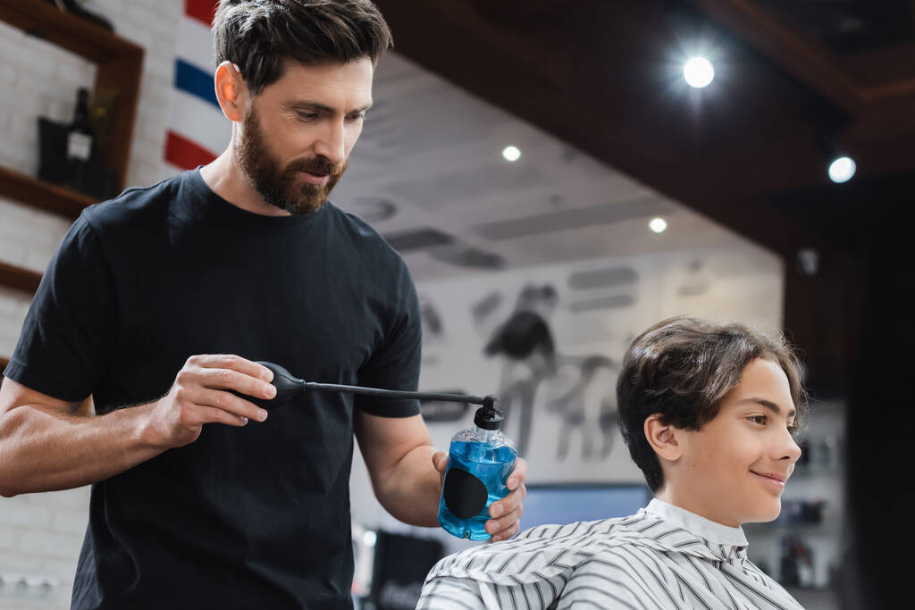 fryzjerka z brodą przy użyciu lakieru do włosów na uśmiechniętym nastolatku w salonie piękności  - Zdjęcie, obraz