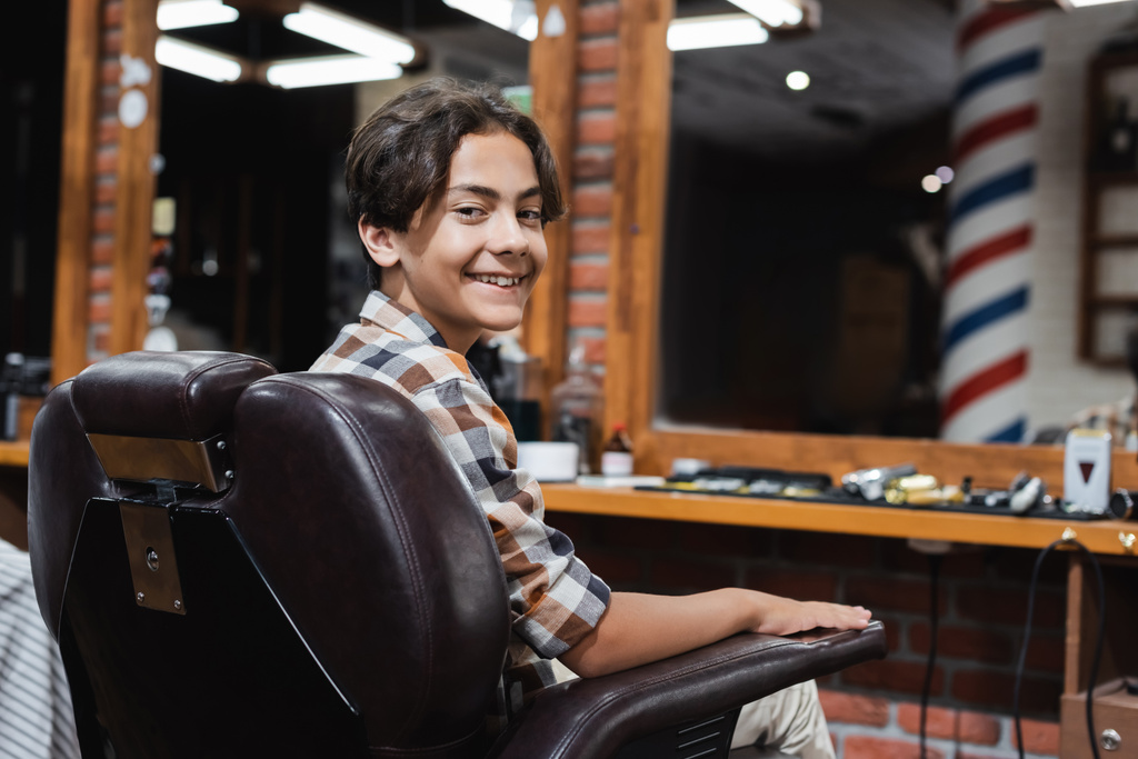Улыбающийся подросток смотрит в камеру, сидя в кресле в салоне красоты  - Фото, изображение