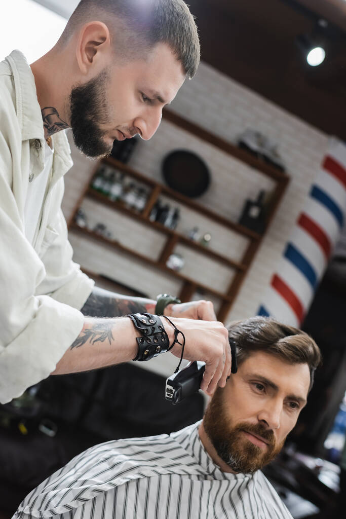Friseur trimmt Haare einer brünetten Kundin im Friseurladen  - Foto, Bild