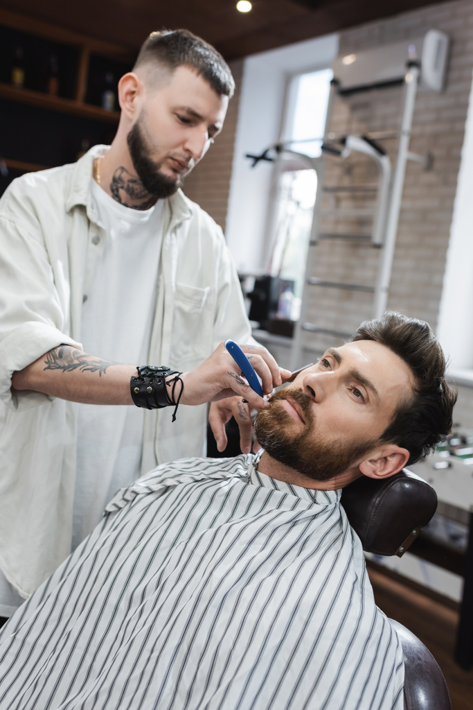 uomo barbuto in mantello parrucchiere vicino barbiere raderlo con rasoio dritto - Foto, immagini